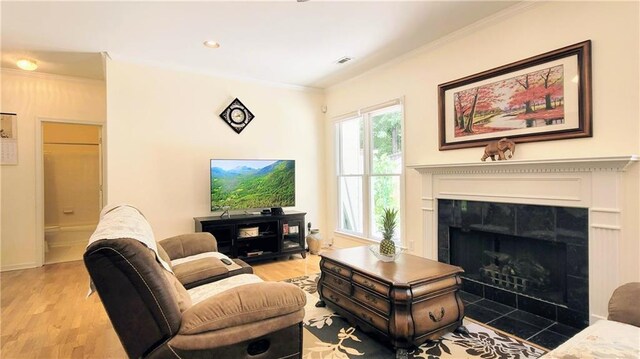 living room featuring light wood-style flooring, a fireplace, visible vents, and crown molding