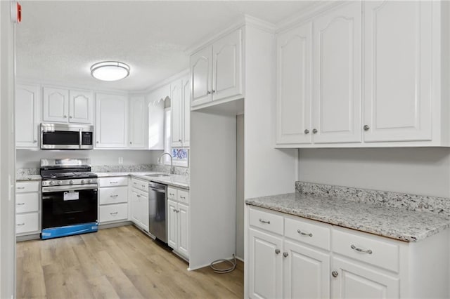 kitchen with a textured ceiling, stainless steel appliances, a sink, light wood-style floors, and white cabinets