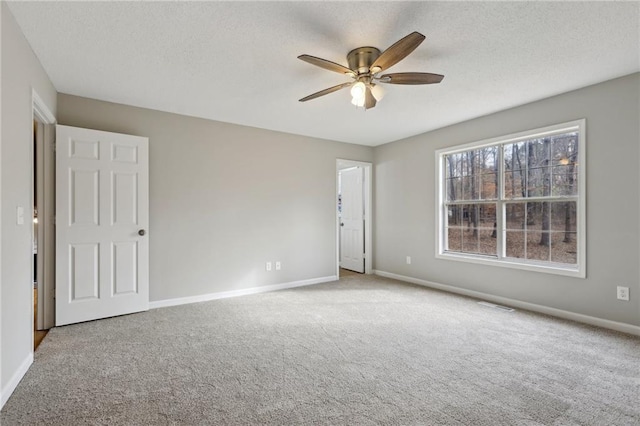 carpeted spare room featuring a ceiling fan, visible vents, baseboards, and a textured ceiling