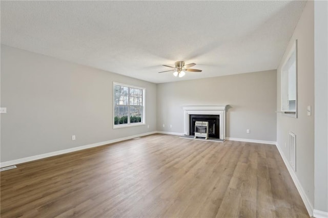 unfurnished living room featuring a glass covered fireplace, a textured ceiling, baseboards, and wood finished floors