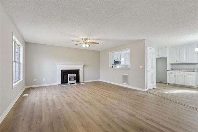 unfurnished living room featuring baseboards, visible vents, a textured ceiling, and light wood finished floors