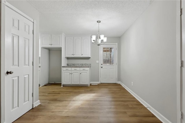 unfurnished dining area with a textured ceiling, light wood finished floors, baseboards, and an inviting chandelier