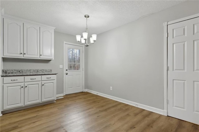 unfurnished dining area with a chandelier, light wood-style floors, a textured ceiling, and baseboards