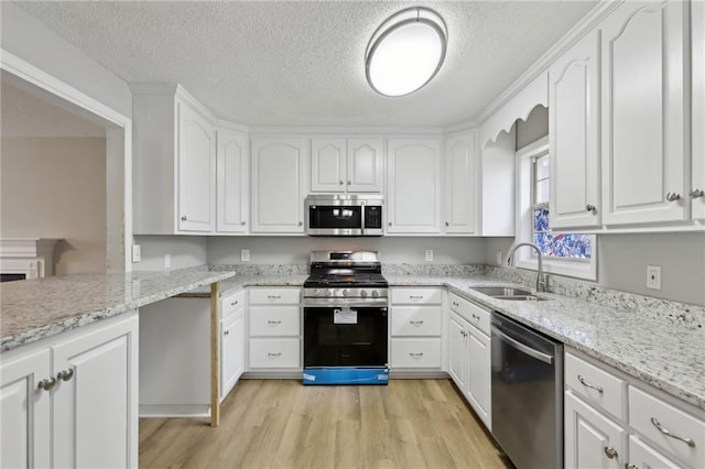 kitchen with appliances with stainless steel finishes, light wood-type flooring, white cabinets, and a sink