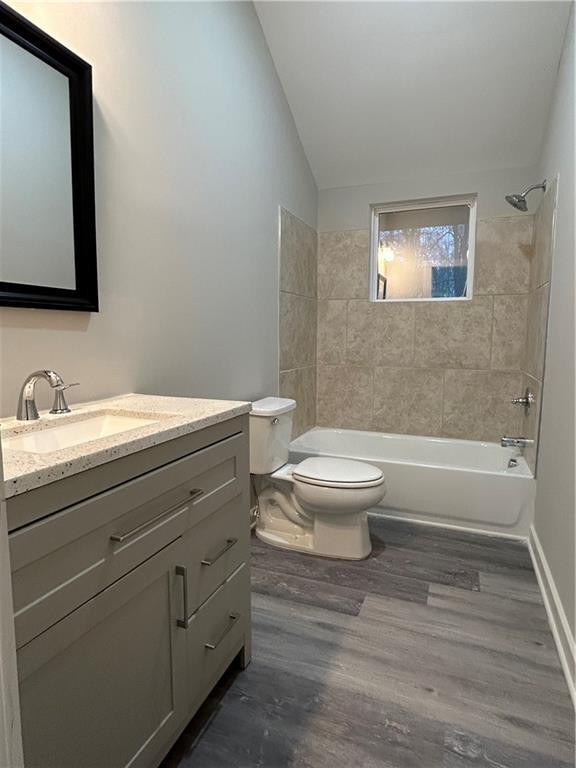 full bathroom featuring vanity, hardwood / wood-style flooring, toilet, tiled shower / bath, and lofted ceiling