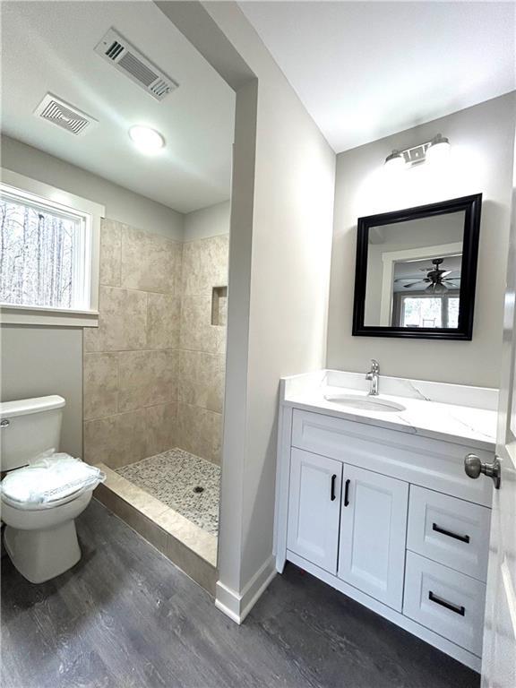 bathroom featuring a tile shower, toilet, vanity, and hardwood / wood-style flooring