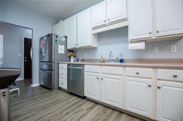 kitchen with appliances with stainless steel finishes, sink, white cabinets, and light hardwood / wood-style floors