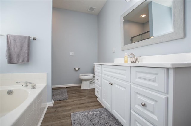 bathroom with toilet, vanity, tiled bath, and hardwood / wood-style floors