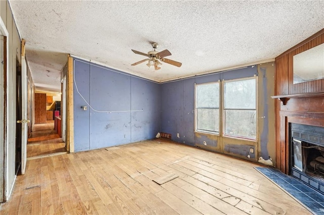 unfurnished living room with ceiling fan, light hardwood / wood-style floors, a textured ceiling, and wood walls