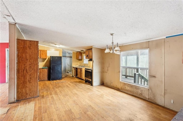 unfurnished living room featuring a notable chandelier, light hardwood / wood-style floors, and a textured ceiling