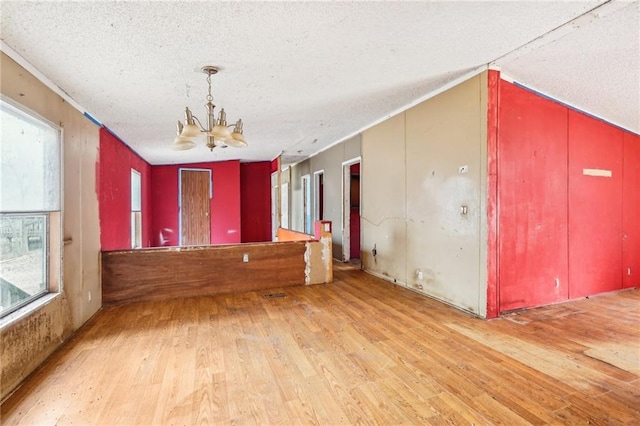 unfurnished room with a healthy amount of sunlight, a notable chandelier, a textured ceiling, and light wood-type flooring