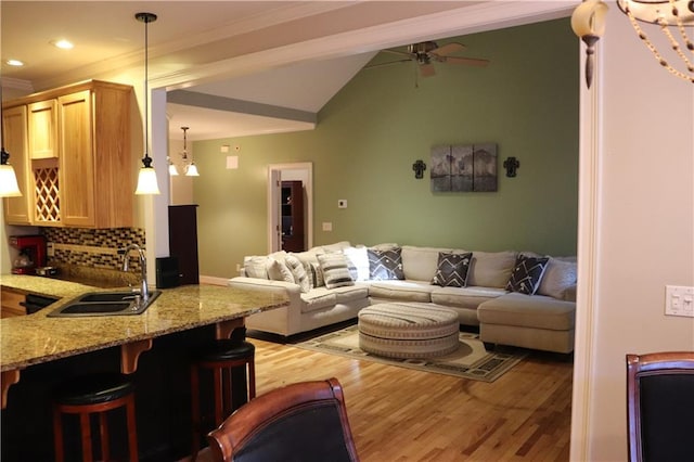 living room featuring light wood-type flooring, lofted ceiling, crown molding, ceiling fan with notable chandelier, and sink