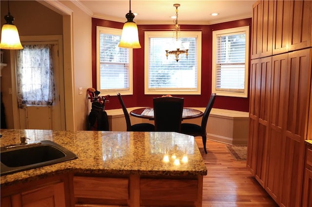 kitchen with sink, ornamental molding, hanging light fixtures, and light hardwood / wood-style floors