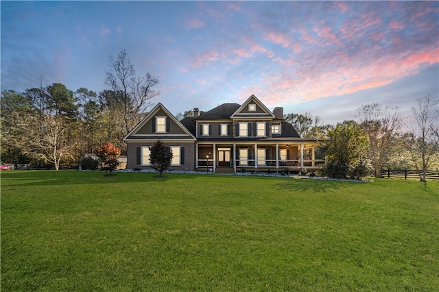 back house at dusk featuring a lawn and covered porch