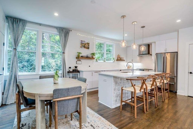 kitchen featuring stainless steel refrigerator, white cabinetry, wall chimney exhaust hood, dark wood-type flooring, and pendant lighting