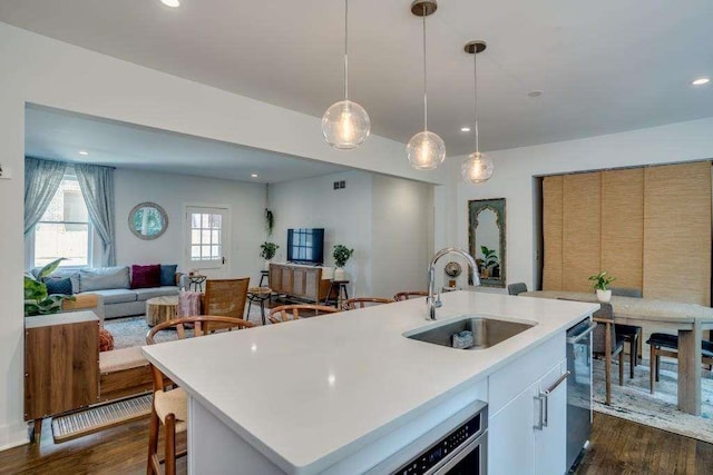 kitchen featuring dishwasher, sink, hanging light fixtures, an island with sink, and dark hardwood / wood-style flooring