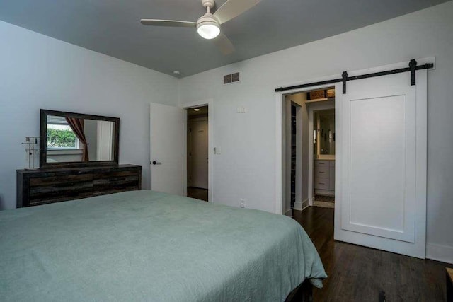 bedroom with dark hardwood / wood-style flooring, a barn door, ensuite bath, and ceiling fan