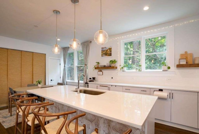 kitchen with white cabinetry, sink, dark hardwood / wood-style flooring, an island with sink, and decorative light fixtures