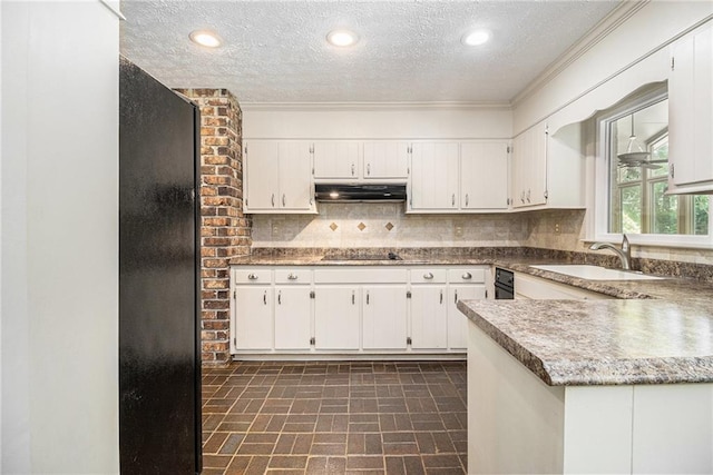 kitchen with under cabinet range hood, black appliances, a textured ceiling, a sink, and brick patterned floors