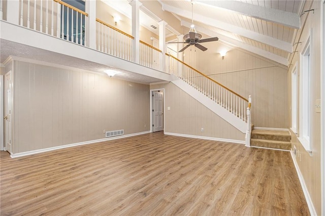 unfurnished living room featuring ceiling fan, wood finished floors, stairs, beamed ceiling, and high vaulted ceiling