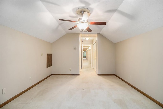 additional living space with a ceiling fan, vaulted ceiling, light colored carpet, and baseboards