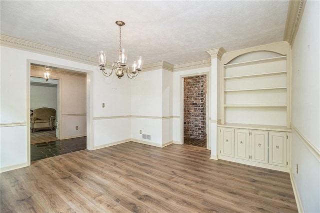unfurnished dining area featuring wood finished floors, a chandelier, a textured ceiling, built in features, and crown molding