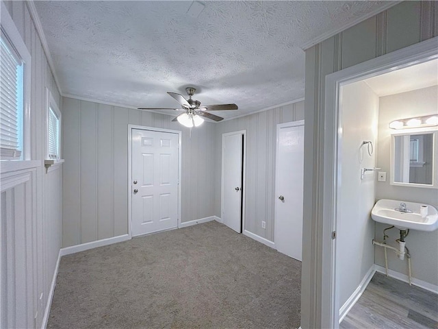 unfurnished bedroom with a textured ceiling, ceiling fan, carpet floors, baseboards, and crown molding