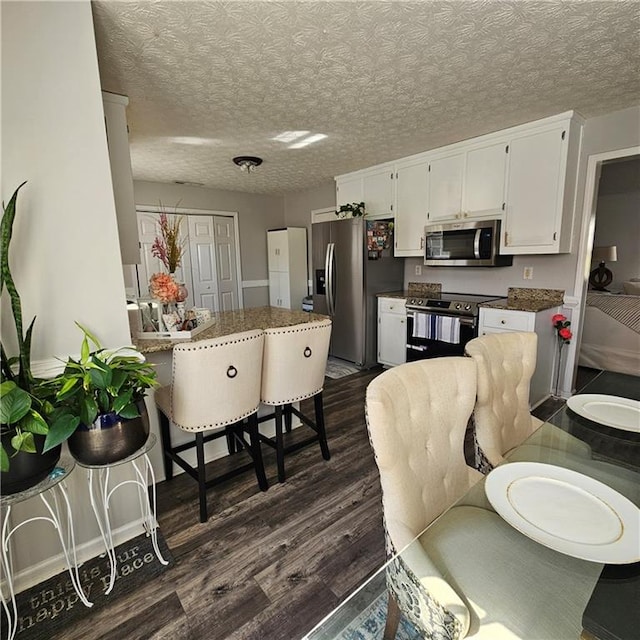 kitchen with dark hardwood / wood-style floors, white cabinets, a kitchen bar, appliances with stainless steel finishes, and a textured ceiling