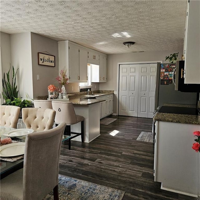 kitchen with white cabinetry, dark stone countertops, a textured ceiling, and dark hardwood / wood-style flooring