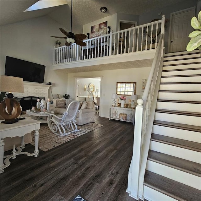 living room with a fireplace, dark hardwood / wood-style flooring, a textured ceiling, high vaulted ceiling, and a skylight