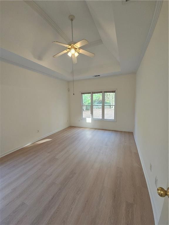 empty room with visible vents, baseboards, a ceiling fan, a tray ceiling, and light wood-style flooring
