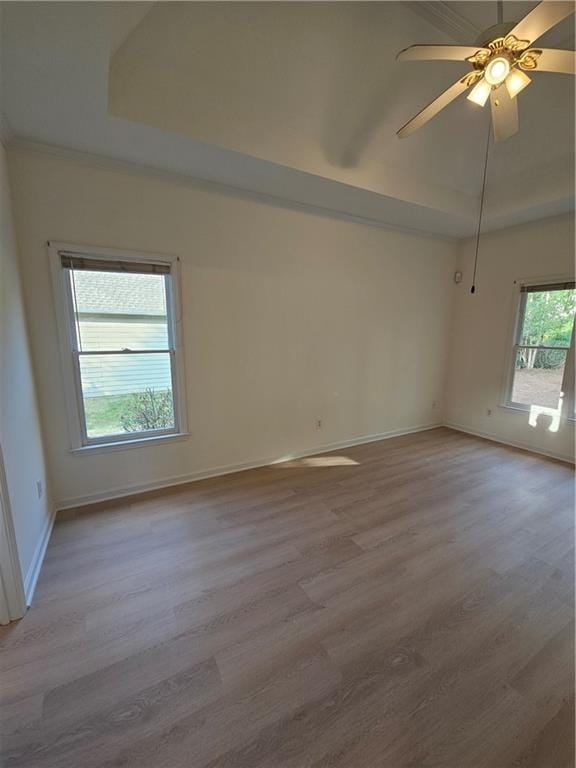 spare room with ceiling fan, light wood-style flooring, baseboards, and a raised ceiling