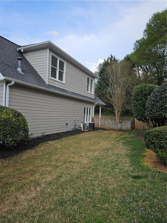view of home's exterior with a yard, fence, a shingled roof, and central air condition unit
