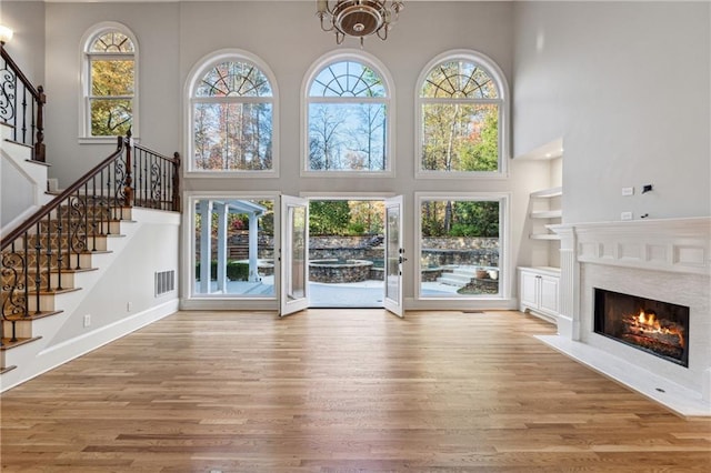 unfurnished living room with built in features, wood-type flooring, a high ceiling, and an inviting chandelier