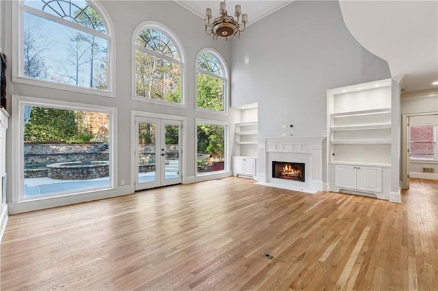 unfurnished living room with built in shelves, a healthy amount of sunlight, a high ceiling, and light wood-type flooring