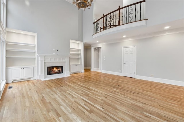 unfurnished living room featuring a notable chandelier, light wood-type flooring, and a towering ceiling