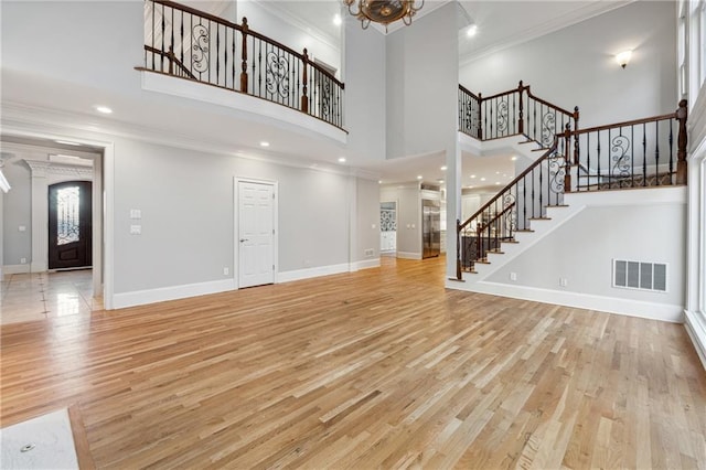 unfurnished living room featuring a notable chandelier, light hardwood / wood-style floors, a towering ceiling, and crown molding