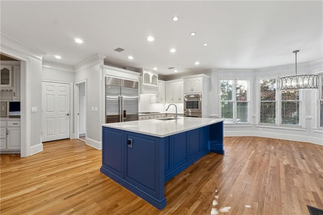 kitchen with appliances with stainless steel finishes, light wood-type flooring, white cabinetry, and ornamental molding