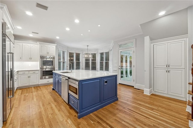 kitchen featuring hanging light fixtures, light wood-type flooring, blue cabinetry, white cabinetry, and stainless steel appliances