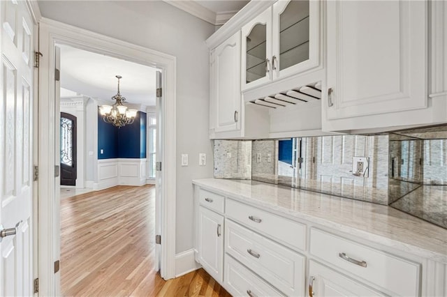 kitchen featuring crown molding, tasteful backsplash, light hardwood / wood-style floors, light stone counters, and white cabinetry