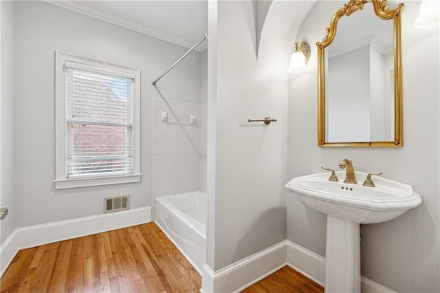 bathroom with hardwood / wood-style flooring, crown molding, and tiled shower / bath