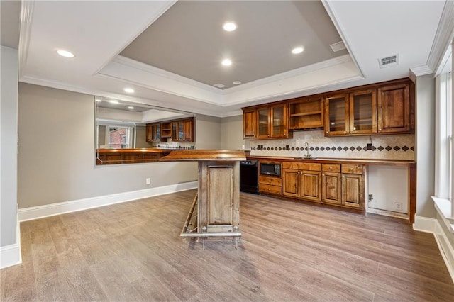 kitchen featuring black microwave, light hardwood / wood-style flooring, backsplash, crown molding, and a breakfast bar area