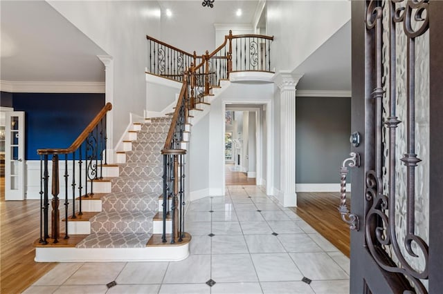 foyer entrance with decorative columns, crown molding, a high ceiling, and light wood-type flooring