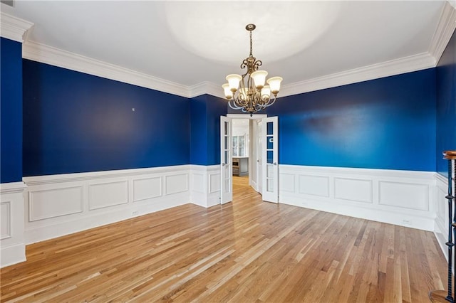 empty room with crown molding, an inviting chandelier, and light wood-type flooring