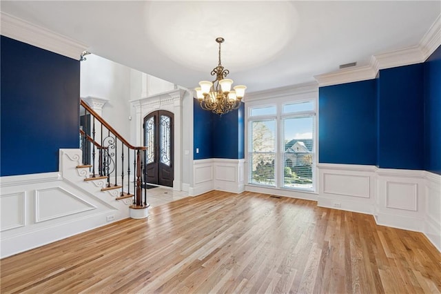 foyer featuring light wood-type flooring, ornamental molding, and an inviting chandelier