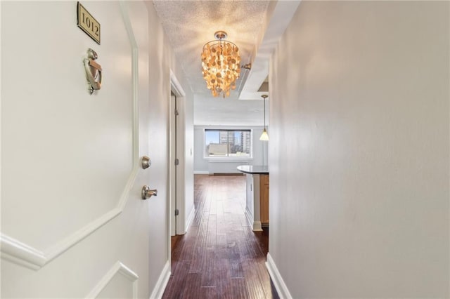 hall with dark hardwood / wood-style floors, a textured ceiling, and a notable chandelier