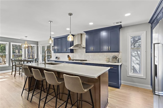 kitchen featuring wall chimney range hood, a sink, decorative backsplash, stainless steel appliances, and a kitchen breakfast bar