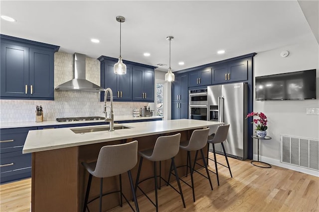 kitchen featuring blue cabinets, visible vents, light wood-style flooring, appliances with stainless steel finishes, and wall chimney exhaust hood