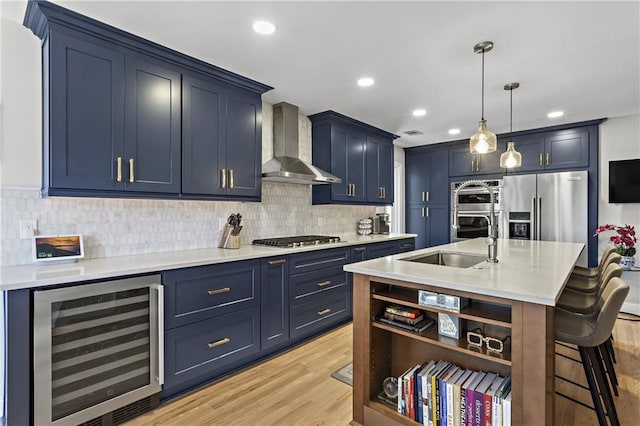 kitchen featuring beverage cooler, a sink, appliances with stainless steel finishes, a breakfast bar area, and wall chimney exhaust hood