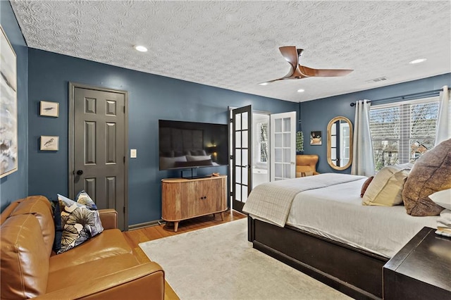 bedroom with a ceiling fan, wood finished floors, visible vents, french doors, and a textured ceiling